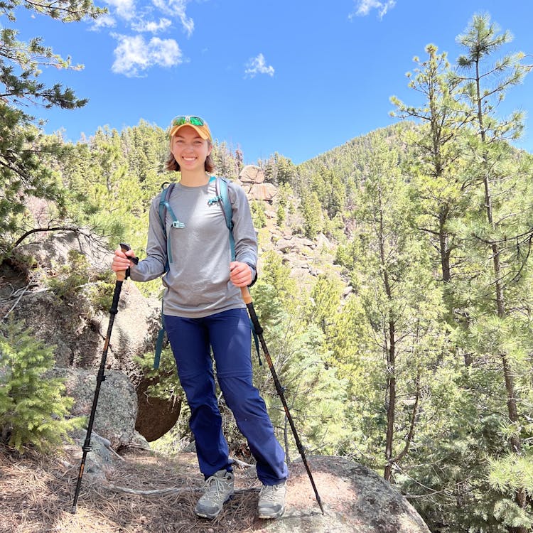 Picture of me in hiking gear with green trees and a blue sky in the background