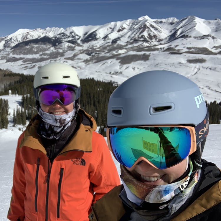 Picture of me and my partner wearing ski gear with snowy mountains in the background
